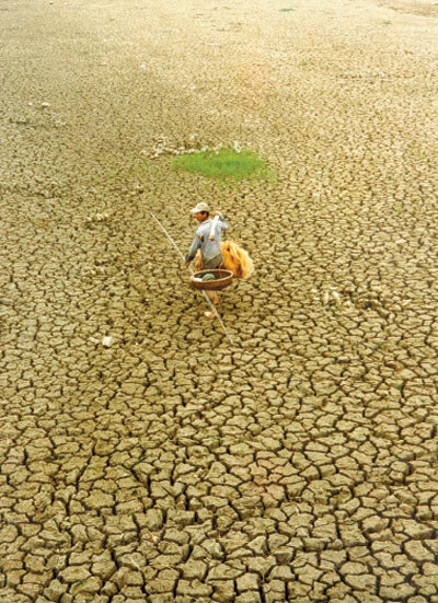 Photo of a fisherman standing in a dry, cracked lake bed.