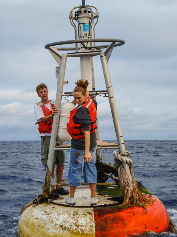 A man and a woman standing on a NOAA marine buoy in the tropical Pacific Ocean