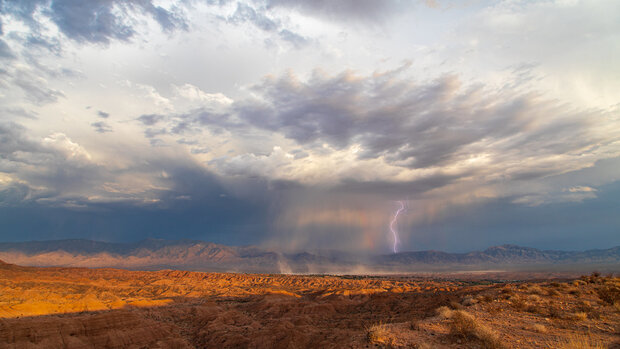 A purple-tinged lightning bolt emerges from a thunderstorm over the desert