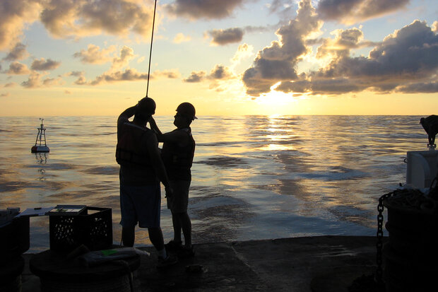 Two people standing on the deck of a ship with a buoy in the background