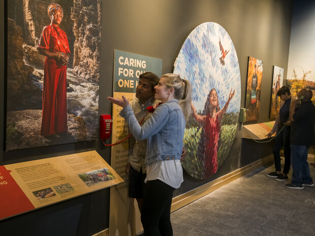 People standing in a museum exhibition observe a displayed image of a person leading climate solutions.