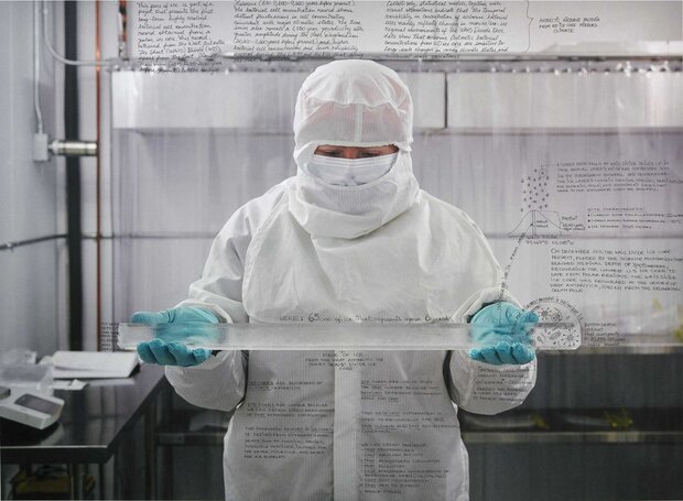 A person with lighter skin wearing a white coverall and blue gloves while holding a narrow cylinder of ice parallel to the ground. Extensive hand-written notes on ice-core research are superimposed on the photograph.