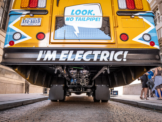 The back of a yellow bus with the words “Look, no tailpipe! I'm electric!” painted on it.