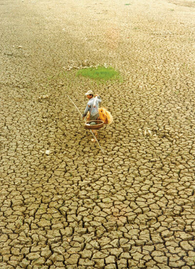 Photo of a fisherman standing in a dry, cracked lake bed.